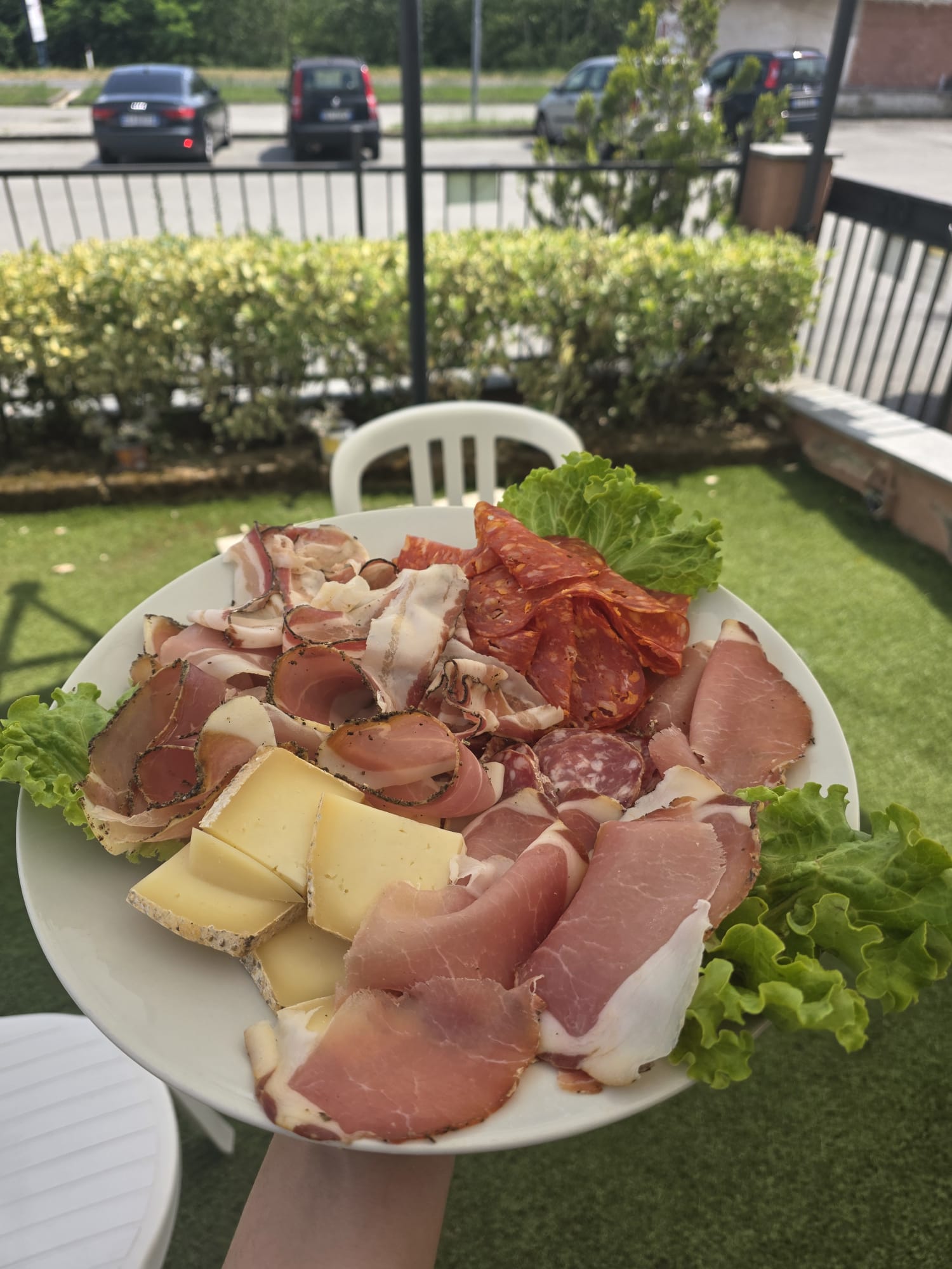 Piatto di Bistro' 90 con prosciutto crudo, salame, formaggio e lattuga, tenuto in mano su un dehors con erba sintetica