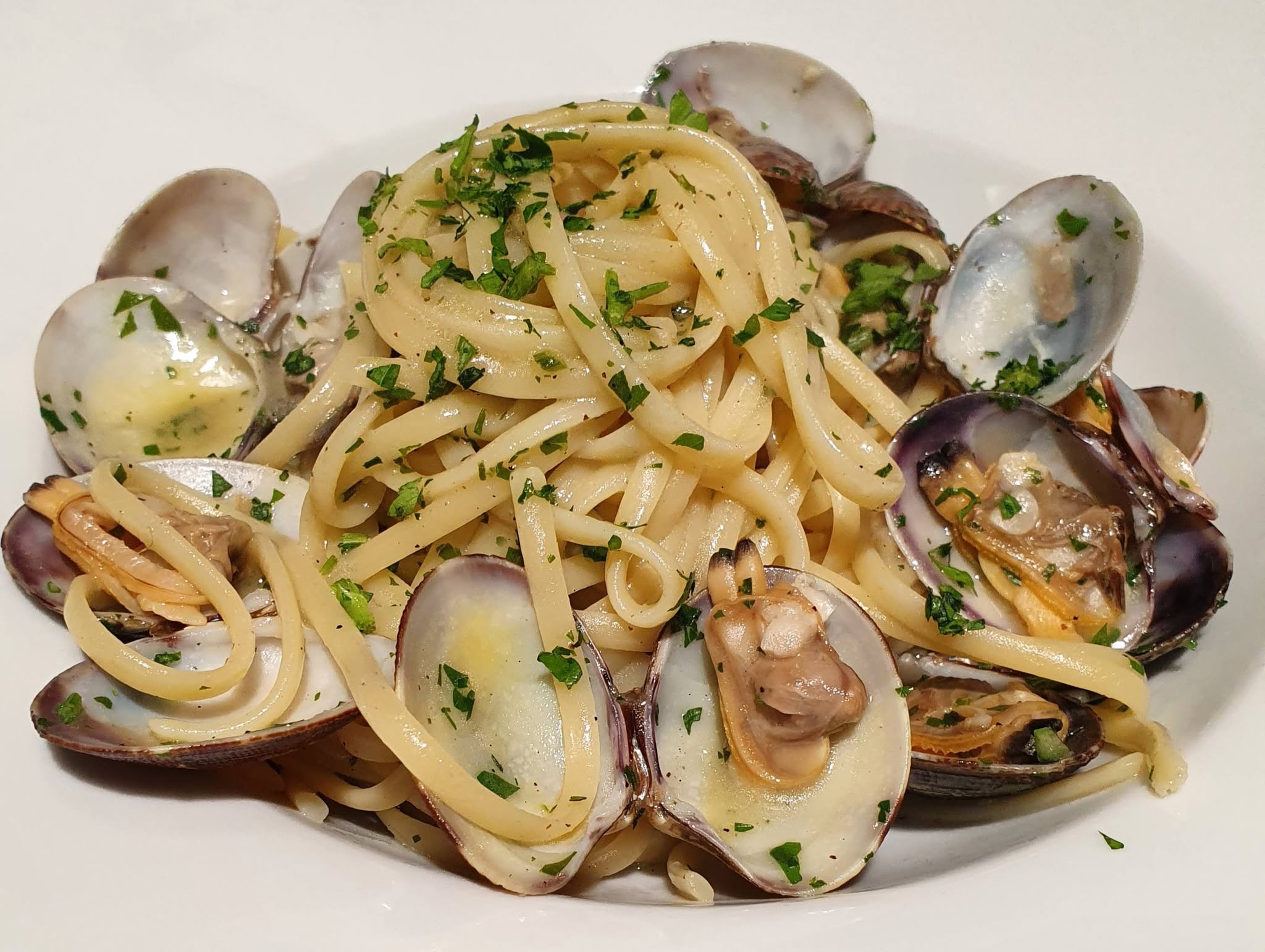Linguine alle vongole con prezzemolo tritato e sugo chiaro in un piatto fondo bianco, primo del Bistro' 90