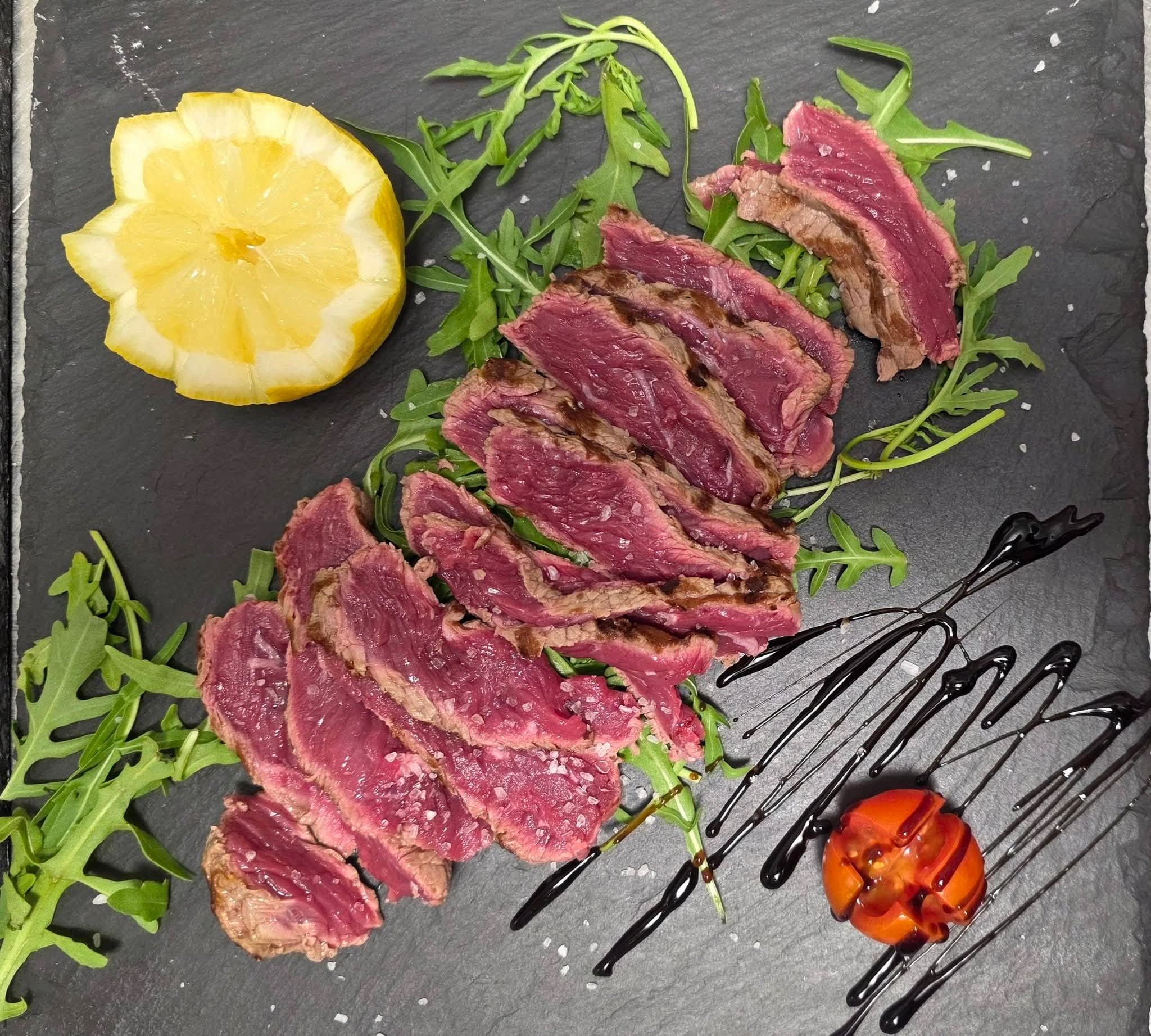 Tagliata al sangue di Bistro' 90 su ardesia con rucola, mezzo limone, sale grosso, pomodorino e glassa balsamica